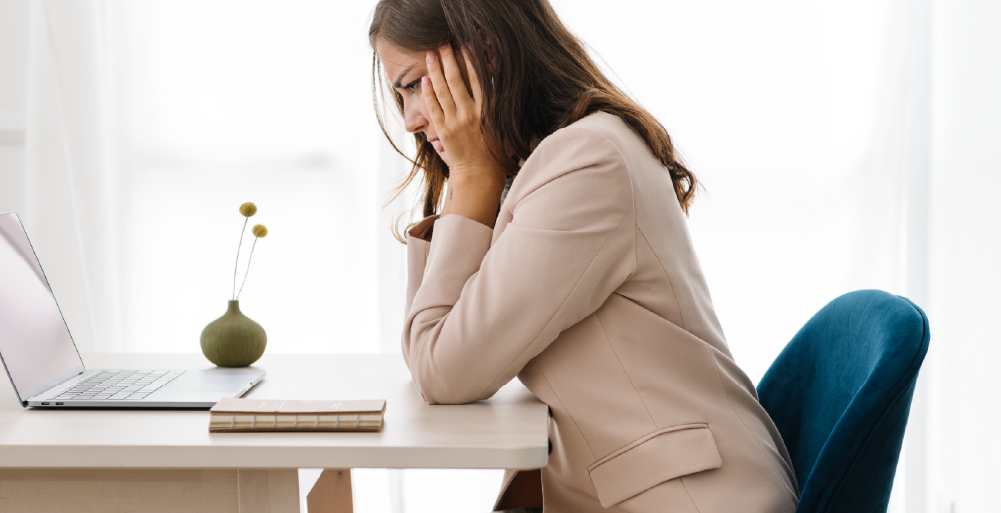 Woman at a desk looking stressed with her head in her hands.